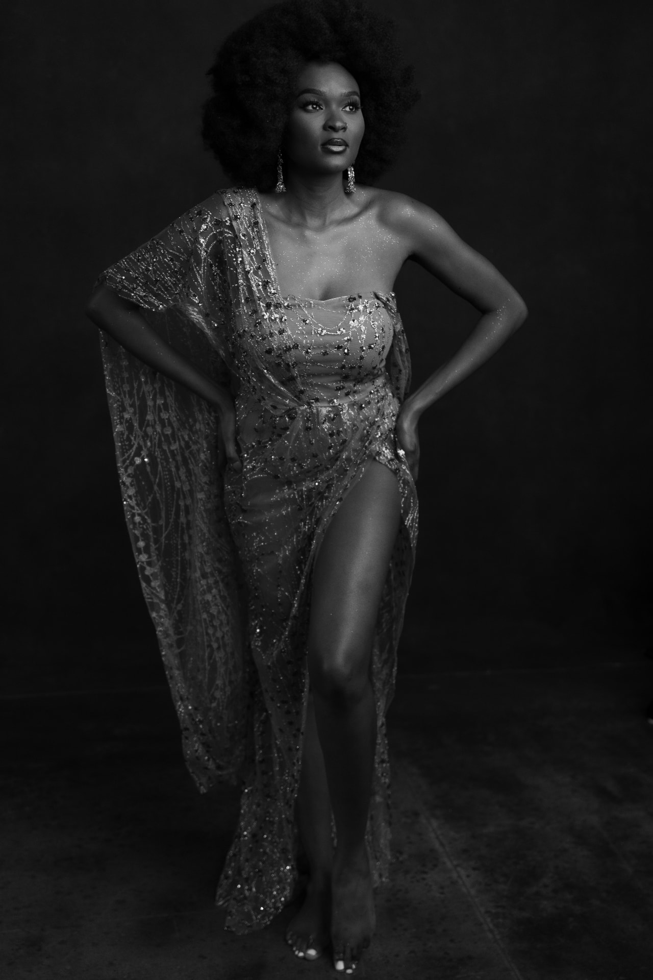 Standing editorial portrait of a woman in a beaded gown, hands on hips, in dramatic studio light